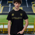 Schwarzes BVB x Guess T-Shirt mit goldfarbenem Guess Jeans Schriftzug und BVB-Emblem, präsentiert im SIGNAL IDUNA PARK.
