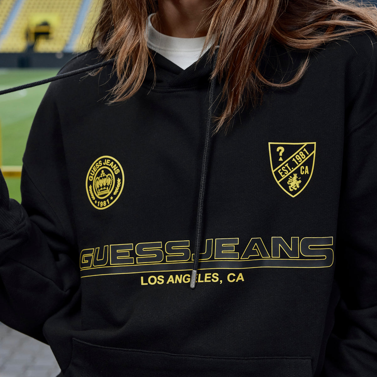 黒いBVB×Guessのフーディ（黄色のロゴ入り）。ボルシア・ドルトムントのファンに最適で、SIGNAL IDUNA PARKで披露されたおしゃれなカジュアルウェアです。