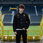 Black BVB x Guess denim jacket featuring the Borussia Dortmund logo and the number 09, modeled by a man at SIGNAL IDUNA PARK.