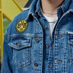Gros plan sur la veste en jean BVB x Guess, de couleur bleue, ornée du logo BVB 09 noir et jaune, présentée au SIGNAL IDUNA PARK.