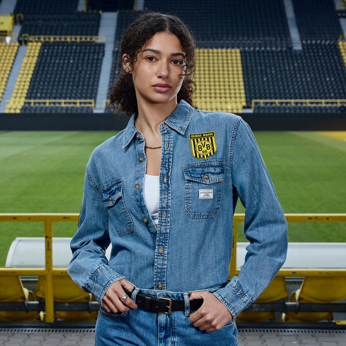 Camicia in jeans blu BVB x Guess da donna, indossata da una modella al SIGNAL IDUNA PARK, con lo stemma del BVB e il logo Guess sul petto.