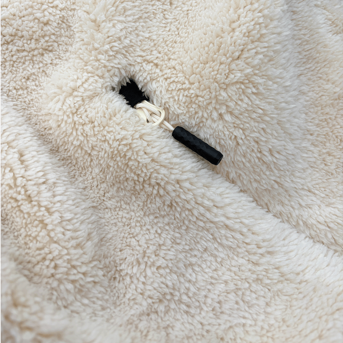 Gros plan sur une veste en polaire Teddy de couleur crème, dotée d'un cordon de serrage et d'une texture douce et moelleuse.