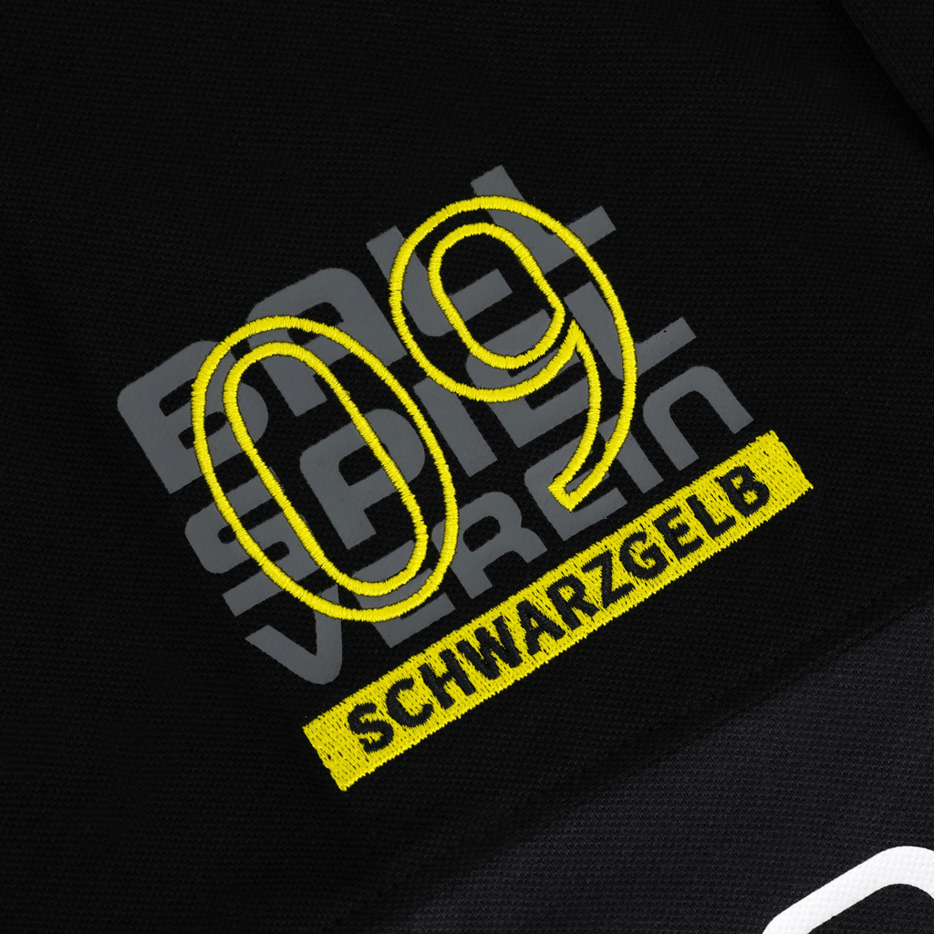 Primer plano de un polo negro del BVB con el logotipo «09» bordado y la inscripción «SCHWARZGELB» en amarillo, ideal para los aficionados del Borussia Dortmund.