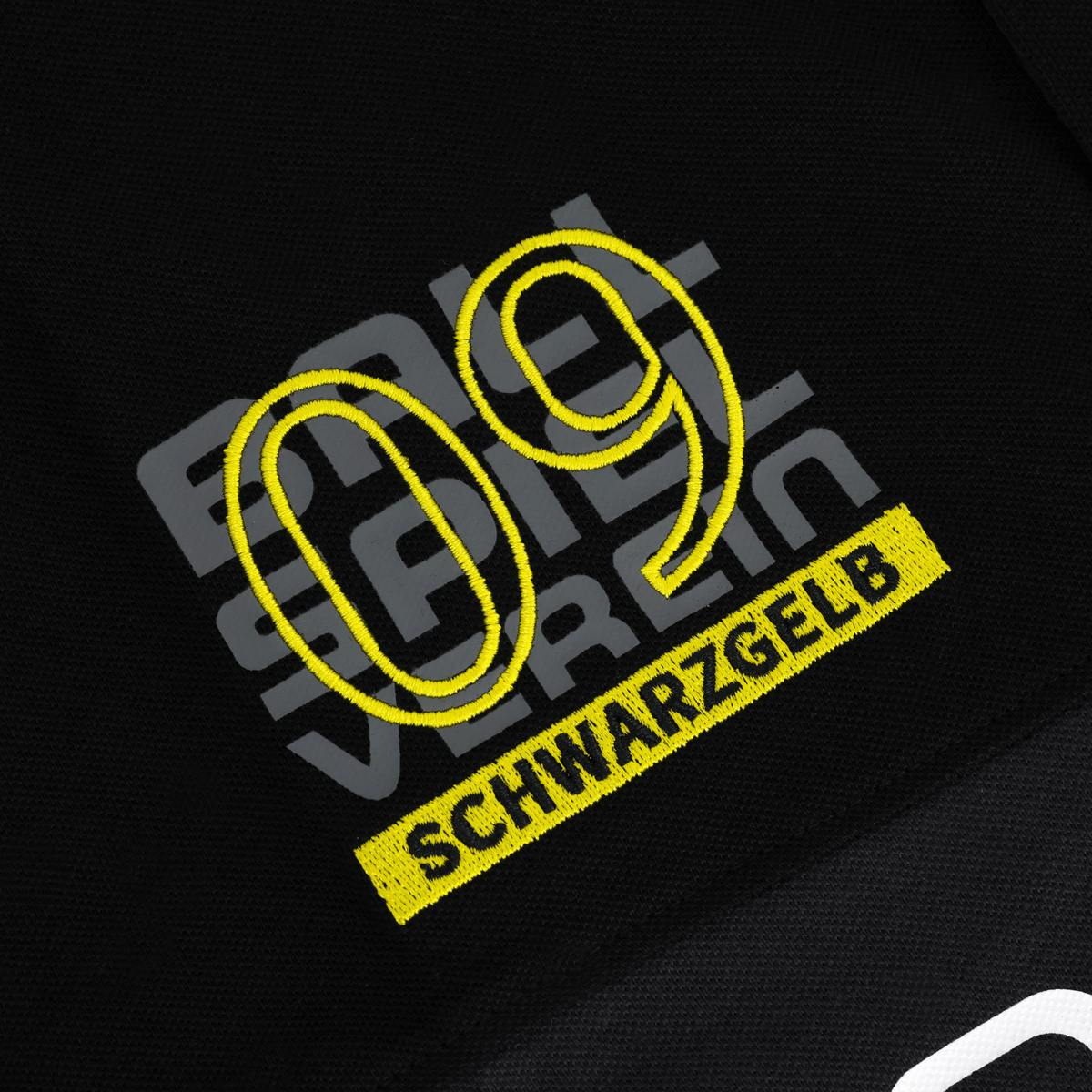 Primer plano de un polo negro del BVB con el logotipo «09» bordado y la inscripción «SCHWARZGELB» en amarillo, ideal para los aficionados del Borussia Dortmund.
