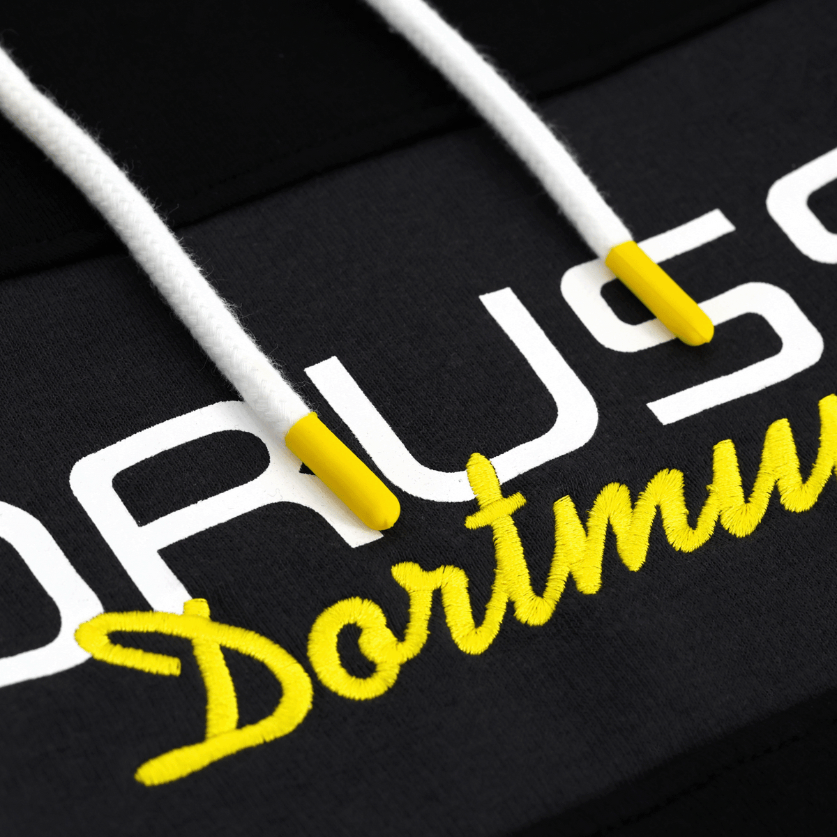 Gros plan sur un sweat à capuche noir du BVB, orné de l'inscription « Dortmund » en jaune et de cordons blancs, idéal comme tenue décontractée pour les supporters du Borussia Dortmund.