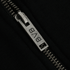 Gros plan sur un curseur de fermeture éclair argenté arborant le logo du BVB, sur une veste de survêtement noire BVB Elements II.