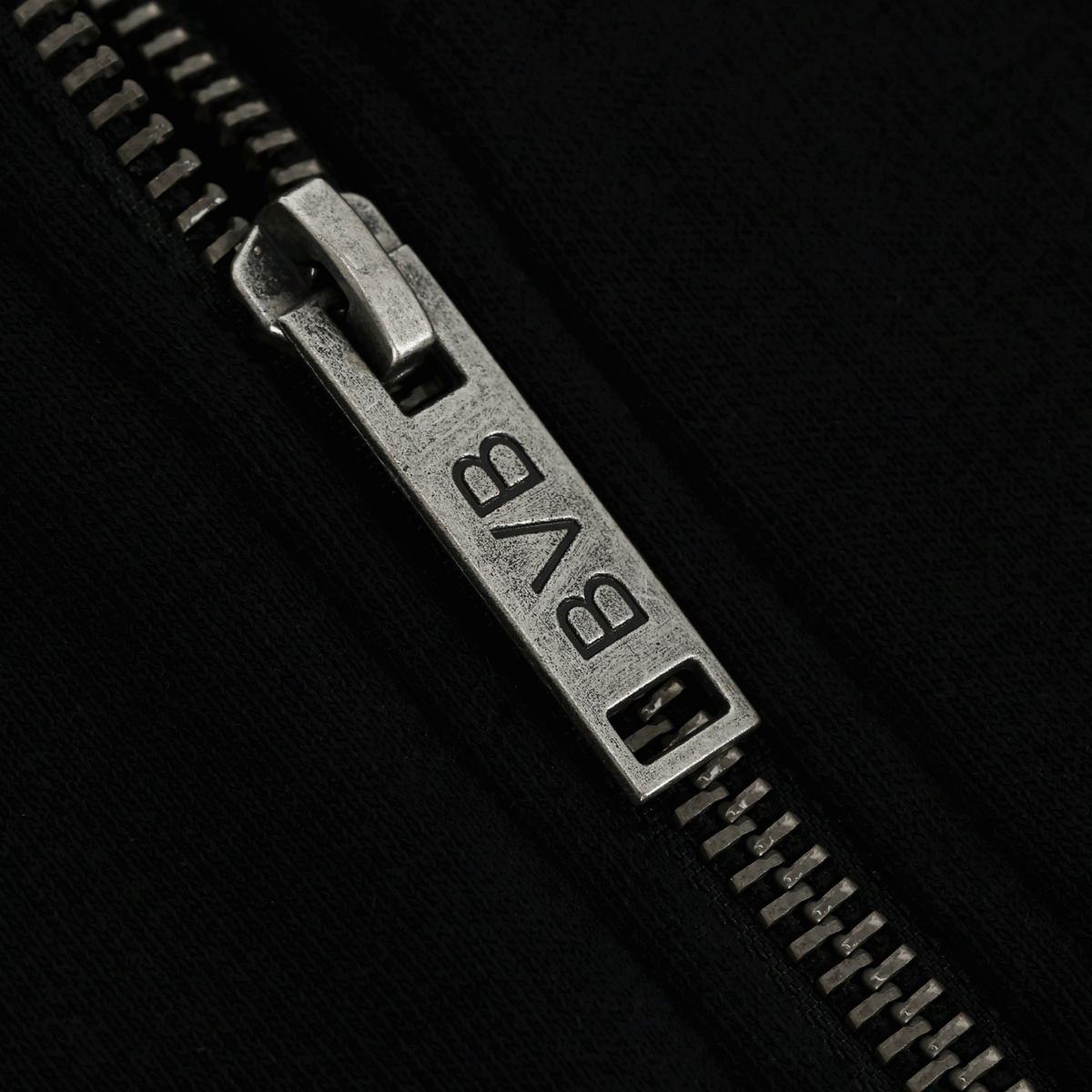 Gros plan sur un curseur de fermeture éclair argenté arborant le logo du BVB, sur une veste de survêtement noire BVB Elements II.