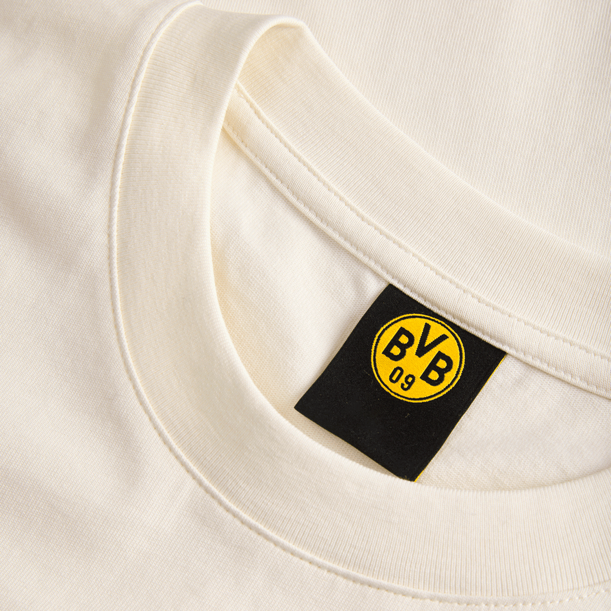 襟の内側に黒い「BVB 09」のロゴが入った、ベージュ色のBVB Tシャツ「Essentials II」の詳細写真。ボルシア・ドルトムントの高品質なファンウェア。