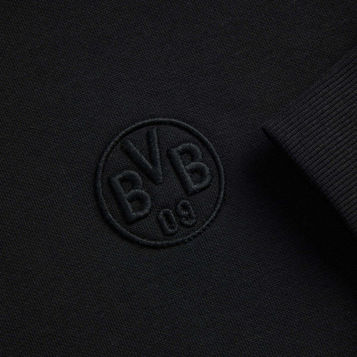 Schwarzer BVB-Hoodie Essentials II mit gesticktem BVB-Logo, Detailaufnahme vom Logo und Ärmel.