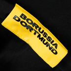 Detailansicht eines schwarzen BVB Hoodies der Essentials II Kollektion mit gelbem Borussia Dortmund Emblem. Idealer Fanartikel für Anhänger von Borussia Dortmund.