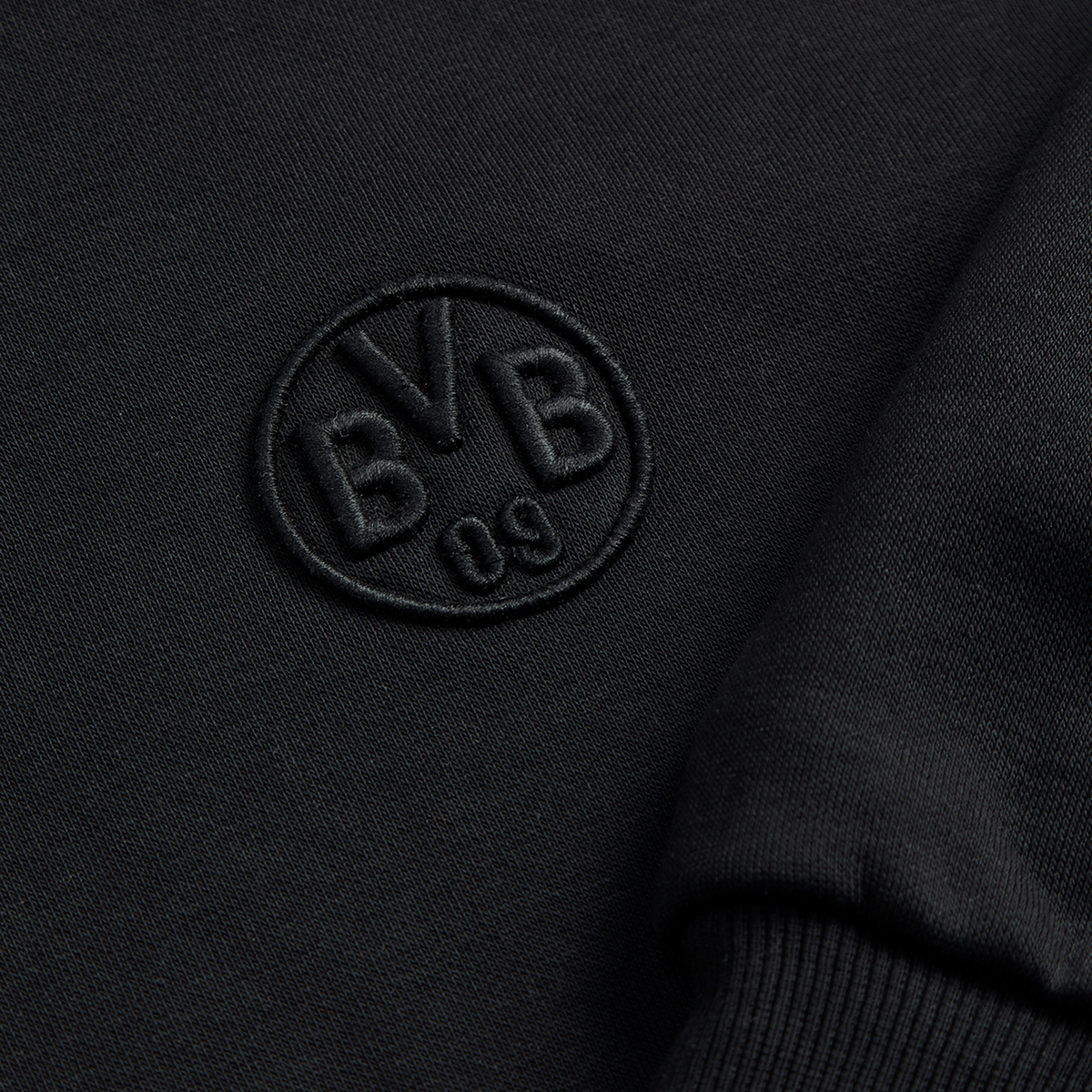 La giacca in felpa nera Essentials II del BVB mostra, in primo piano, il logo BVB 09 ricamato: un elegante capo imperdibile per i tifosi del Borussia Dortmund.