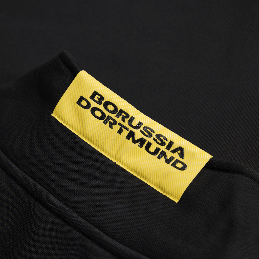 Primer plano del jersey negro Essentials II del BVB con el logotipo amarillo del Borussia Dortmund en la parte delantera.