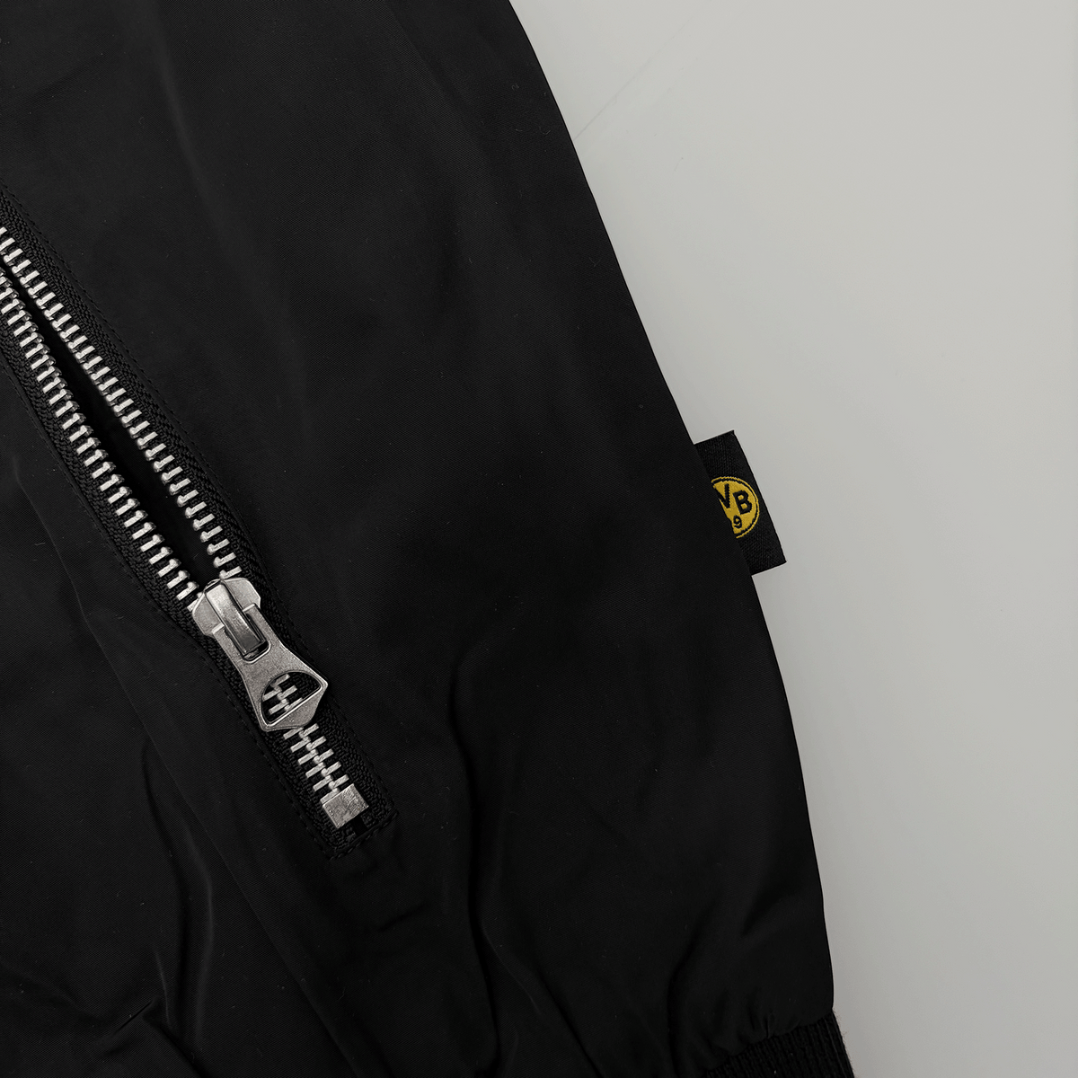 ジッパーが表に出ている、黒と黄色のBVBラベルが付いた「Essentials II」のBVBジャケットのクローズアップ。