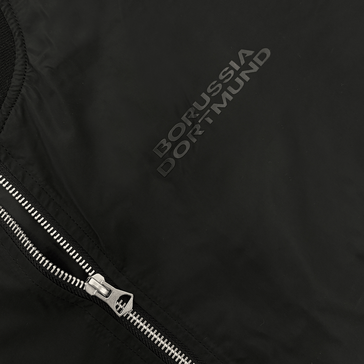 ジッパー付きでボルシア・ドルトムントのロゴが入った、ブラックのBVBジャケット「Essentials II」の詳細画像。