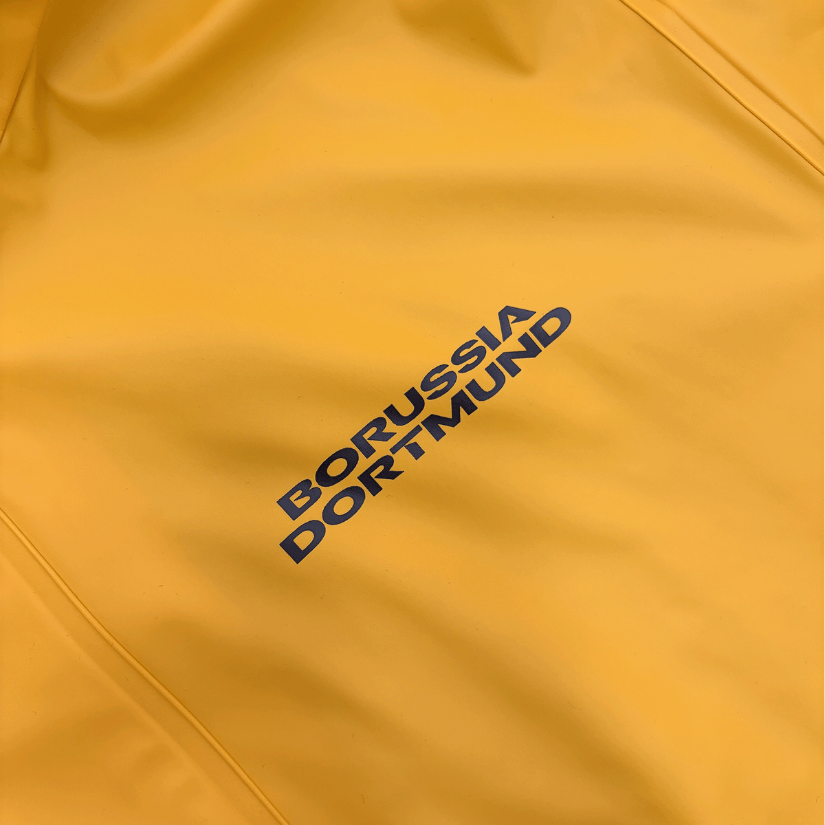 Vista dettagliata dell'impermeabile giallo Essentials II del BVB con la scritta "Borussia Dortmund" in diagonale.