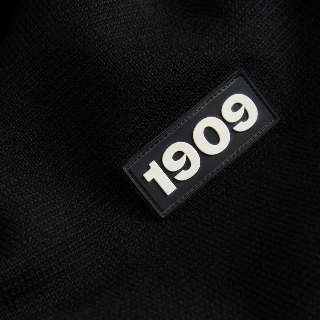 Primo piano di un capo tessile del BVB di colore nero con lo stemma “1909” in rilievo di colore bianco.