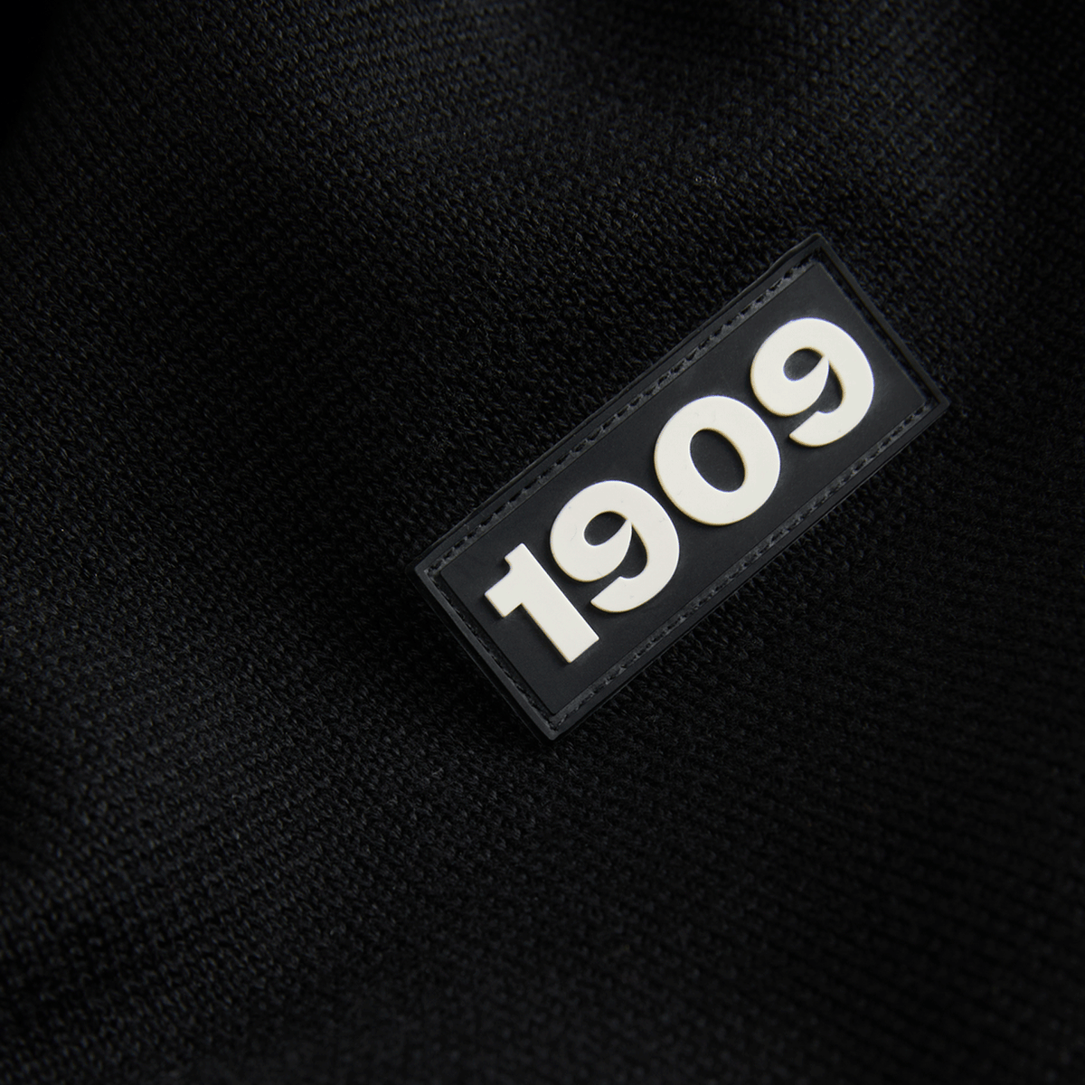 Primo piano di un capo tessile del BVB di colore nero con lo stemma “1909” in rilievo di colore bianco.