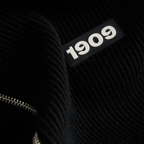 Schwarzer Strickstoff mit eingeprägtem 1909 Schriftzug und sichtbarem Reißverschluss in Nahaufnahme.