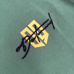 Nahaufnahme eines BVB T-Shirts Lifestyle in Duckgreen mit prominentem gelben BVB-Logo und schwarzer Signaturstickerei.