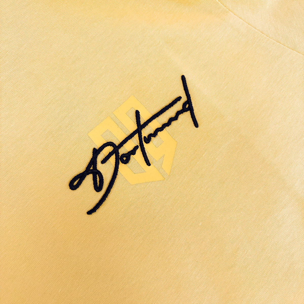 Gelbes Textil mit Dortmund-Schriftzug und geometrischem Logo, Detailaufnahme für BVB-Fanshop.