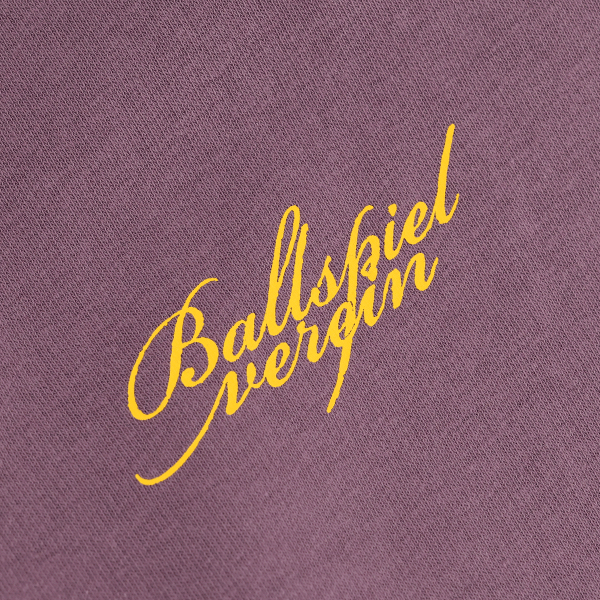 Violetter BVB Hoodie mit gelbem Ballspielverein-Schriftzug in geschwungener Schriftart, Nahaufnahme eines Details auf dem Stoff.
