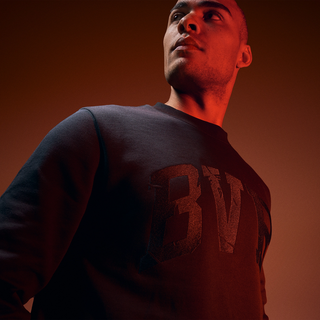 Pull noir BVB Heat II avec un grand logo BVB sur le devant, présenté par un mannequin en gros plan, idéal pour les supporters du Borussia Dortmund.