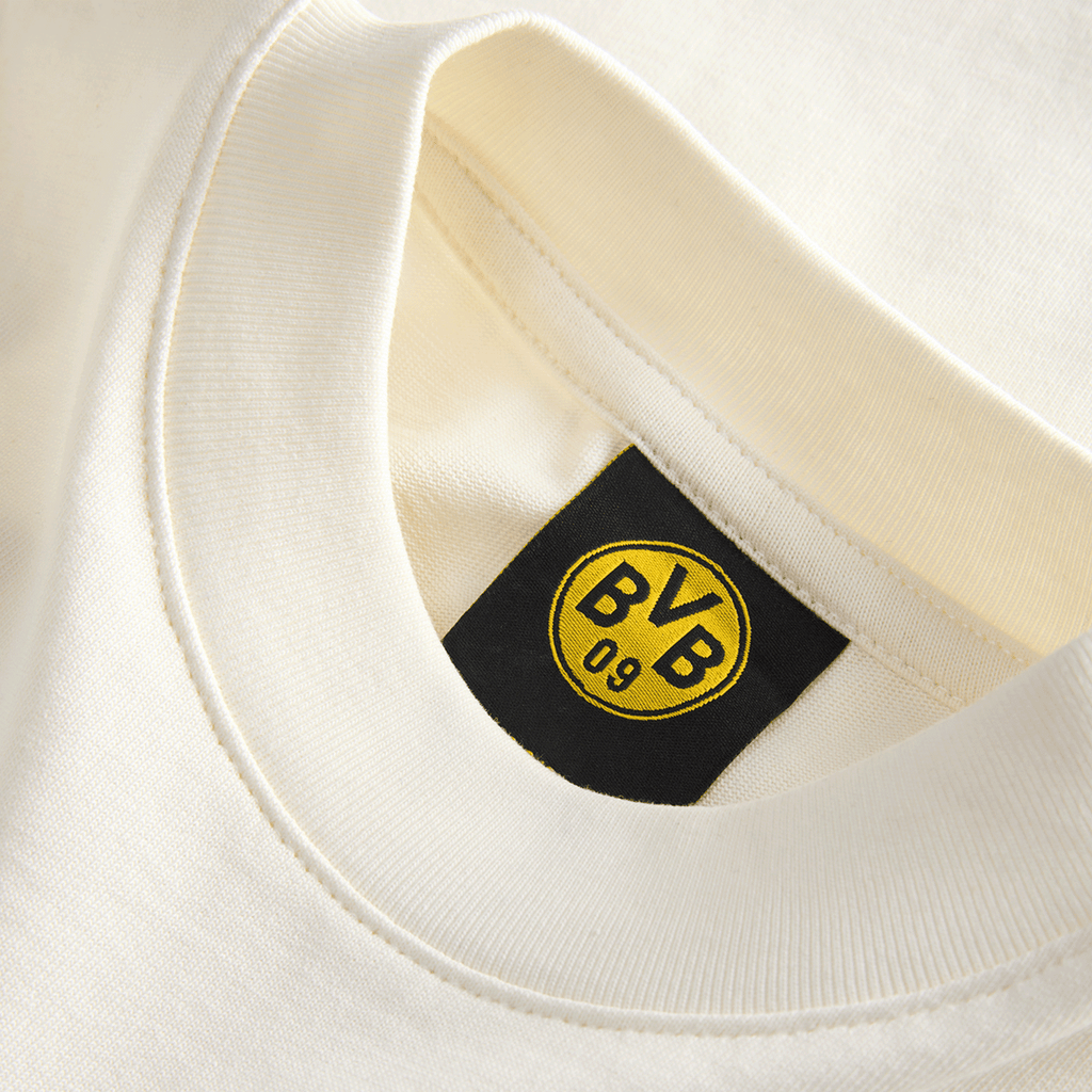 Primer plano de una camiseta infantil del BVB de color beige, de la colección Essentials II, con el logotipo «BVB 09» en la etiqueta interior