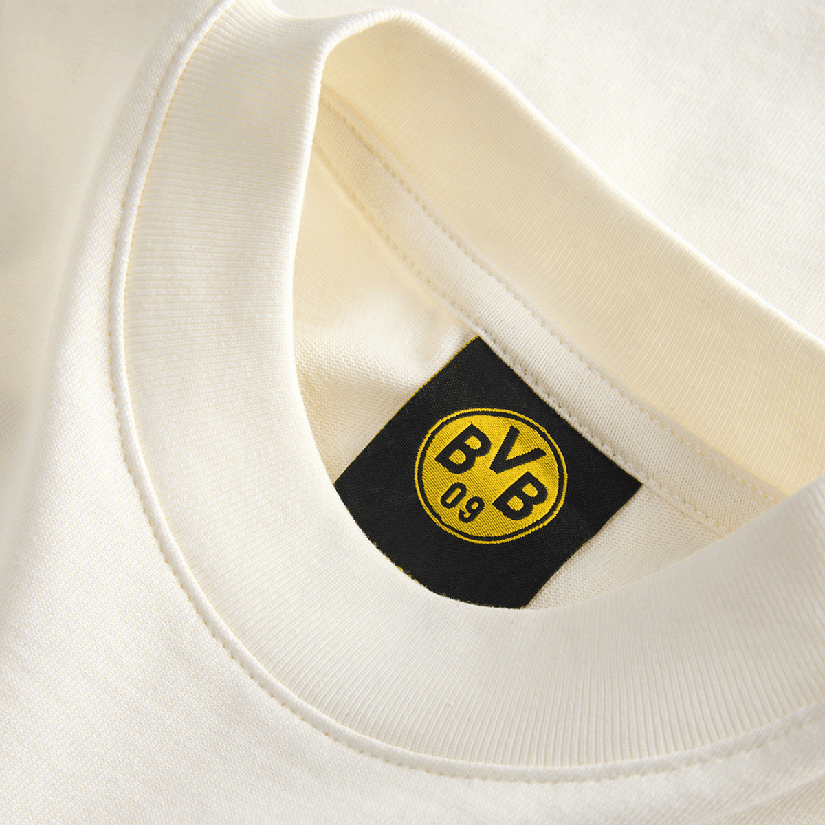 Primer plano de una camiseta infantil del BVB de color beige, de la colección Essentials II, con el logotipo «BVB 09» en la etiqueta interior
