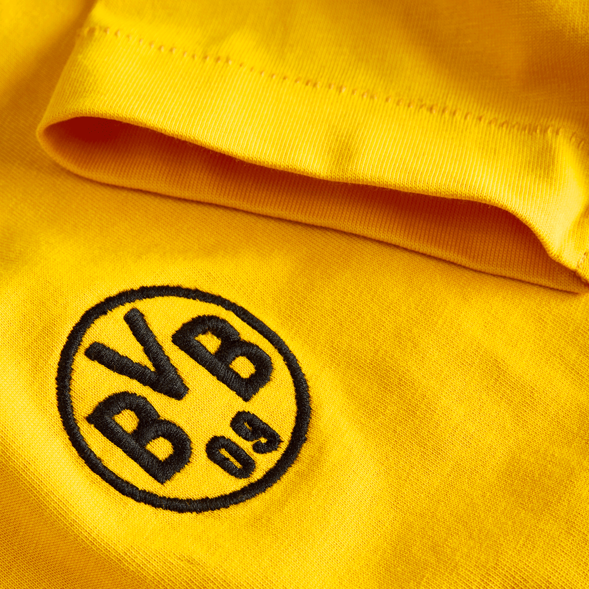 Primer plano de una camiseta amarilla del BVB de la colección Essentials II para niños, con el logotipo del BVB 09 bordado en negro.