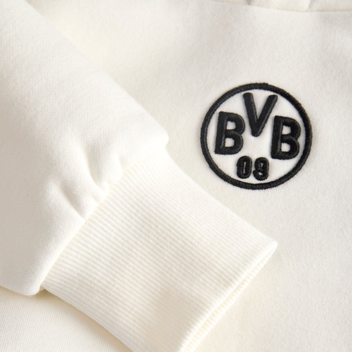 BVBの刺繍ロゴとリブ編みの袖口が特徴の、キッズ用ベージュのBVBフーディー「Essentials II」のディテール写真。