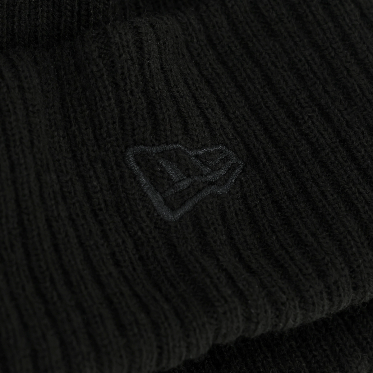 Gros plan sur un tissu noir orné d'un logo brodé, sur fond sombre