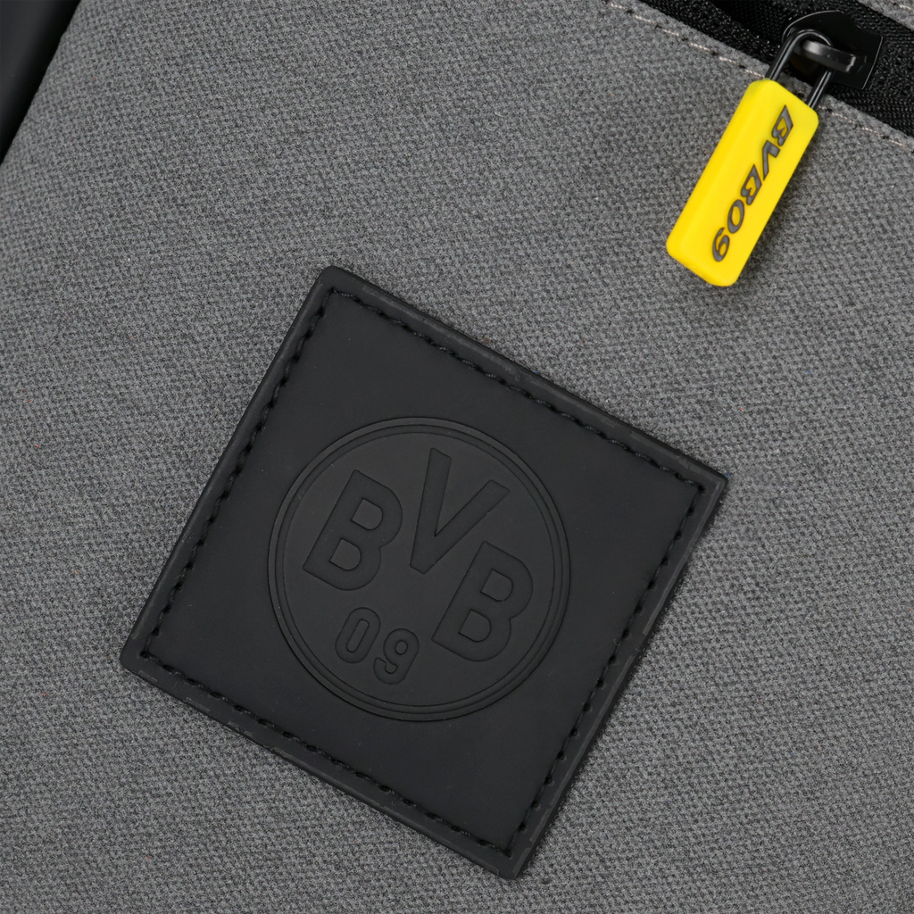 Detailansicht einer grauen BVB-Schultertasche mit schwarzem BVB-Logo und gelbem Reißverschlussanhänger.