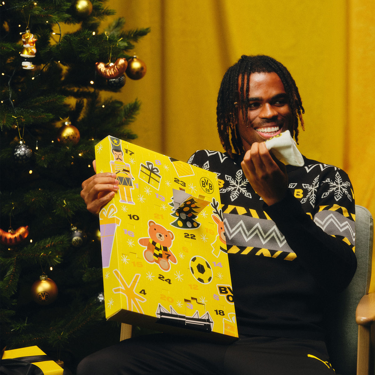 BVB-Sockenkalender 2026 in schwarzgelbem Design, gehalten von einer lächelnden Person neben einem Weihnachtsbaum.