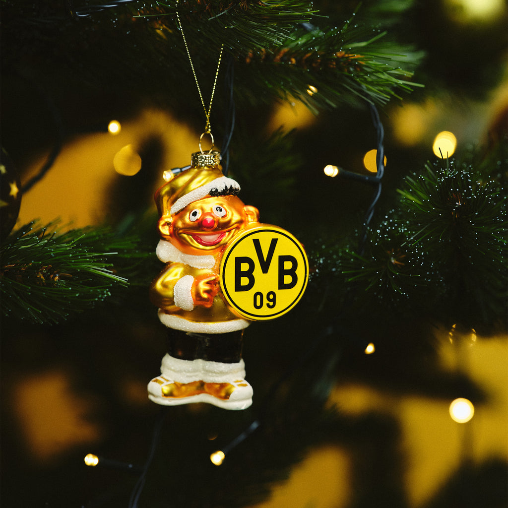 Goldfarbener BVB-Weihnachtsanhänger in Form von Ernie mit gelbem BVB 09 Logo aus Glas, weihnachtlich dekoriert, an einem grünen Weihnachtsbaum aufgehängt.