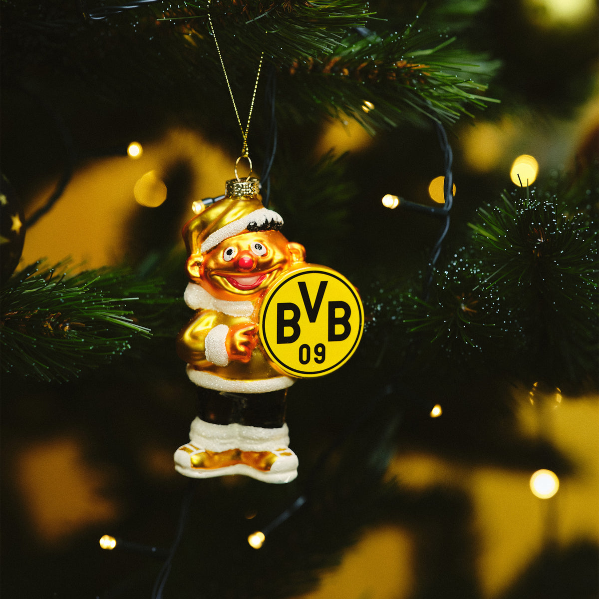 Goldfarbener BVB-Weihnachtsanhänger in Form von Ernie mit gelbem BVB 09 Logo aus Glas, weihnachtlich dekoriert, an einem grünen Weihnachtsbaum aufgehängt.