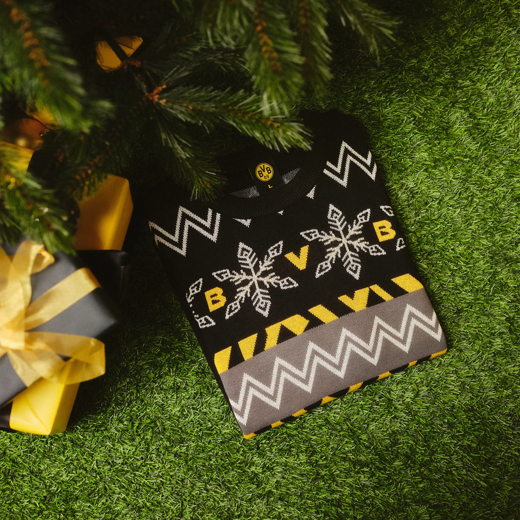 Winterpullover im Norweger-Design von Borussia Dortmund mit BVB-Logo und Schneeflocken, in schwarzgelben Farben unter einem Weihnachtsbaum arrangiert.