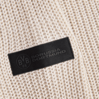 Beiger BVB-Winterpullover in Nahaufnahme, mit schwarzem Borussia Dortmund-Logo auf einem Etikett auf der Vorderseite des Strickstoffs.