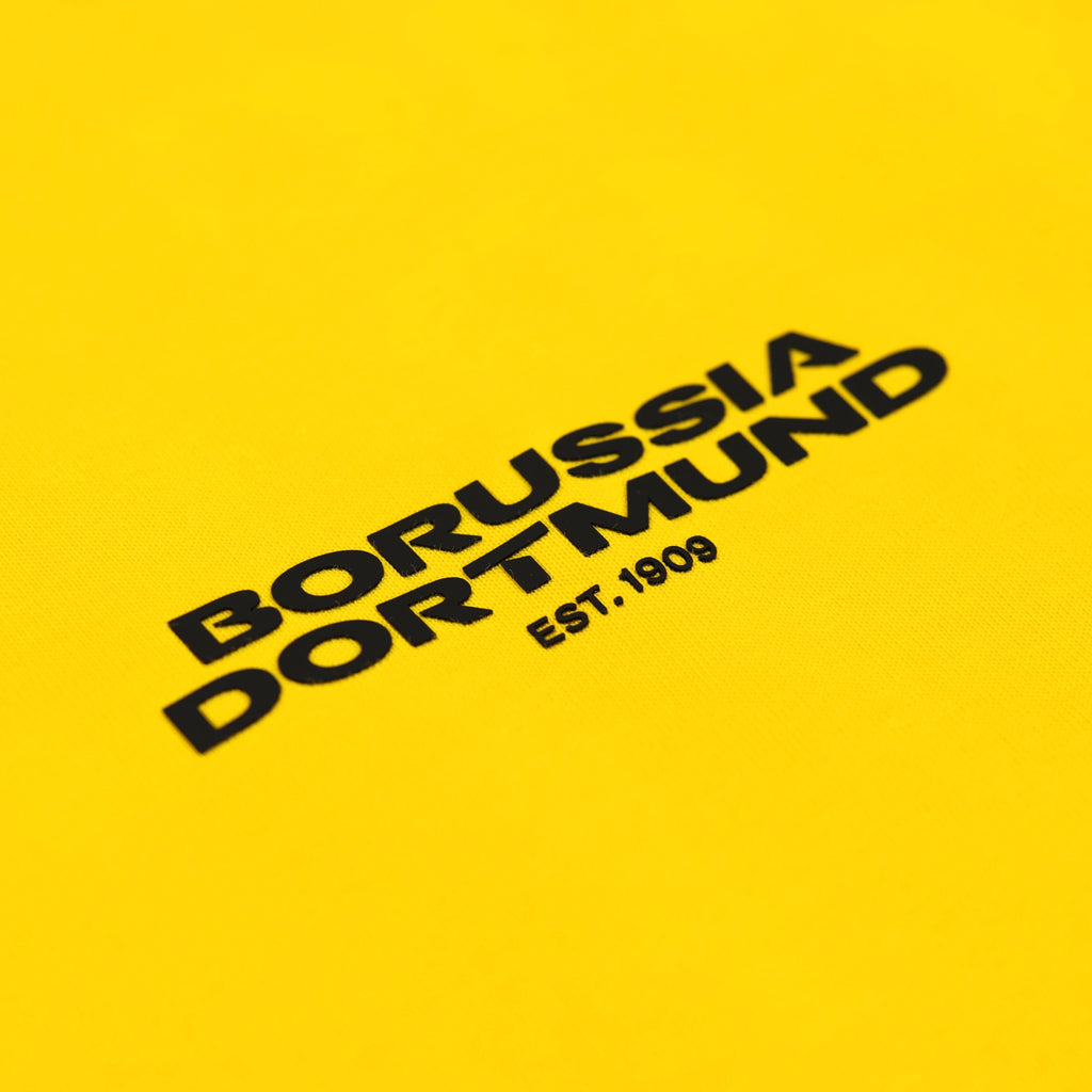 Nahaufnahme eines gelben BVB Urban Tee Spectra mit schwarzem Borussia Dortmund Logo und Schriftzug 'EST. 1909'.