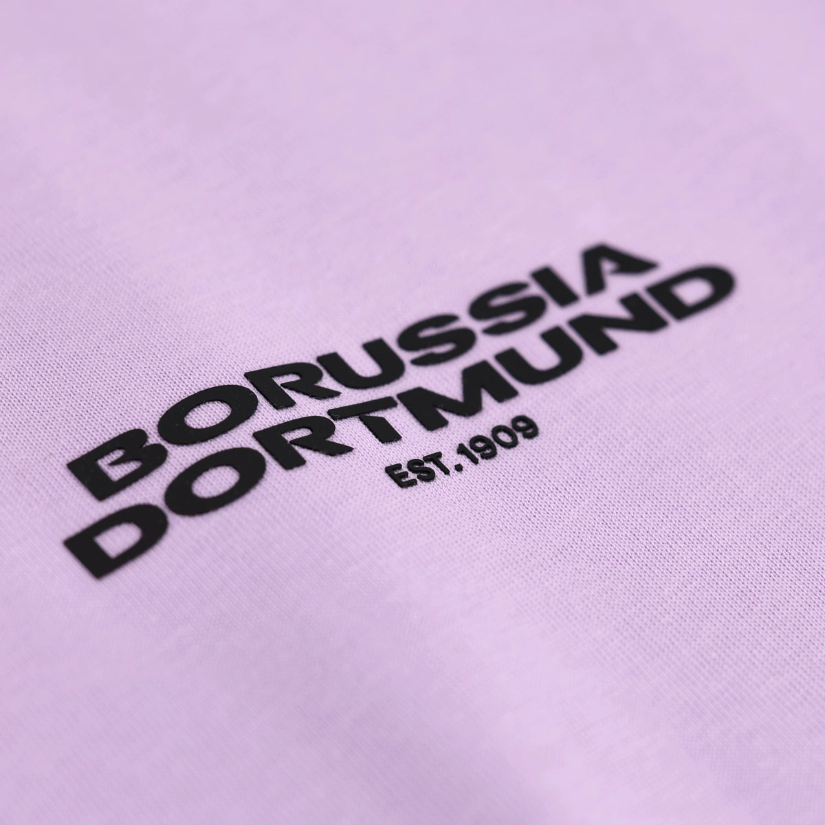 Lila BVB-T-Shirt mit schwarzem Borussia Dortmund-Schriftzug und Est. 1909, detailreiche Nahansicht des Motivs.
