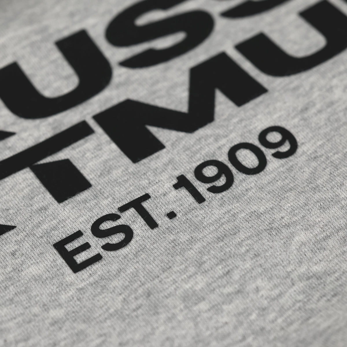 Detailaufnahme eines grauen BVB Urban Hoodies mit schwarzem Borussia Dortmund Schriftzug und 'EST. 1909' Aufdruck.