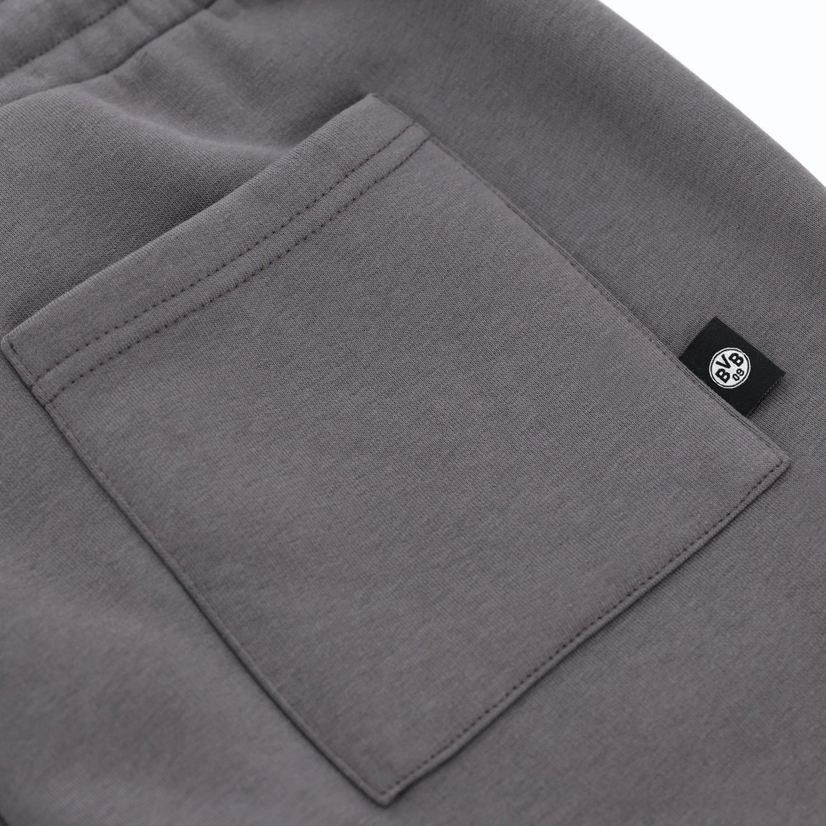 Graue BVB Urban Sweatshorts in der Detailansicht mit Tasche und schwarzweißem BVB-Logo, ideal als Fanartikel oder Streetwear geeignet.
