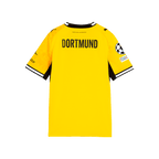 La imagen muestra la vista trasera de la camiseta amarilla de local del BVB para la temporada 26-27 para niños, con la inscripción «DORTMUND», el logotipo de PUMA y el logotipo de la Liga de Campeones en la manga.