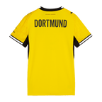La camiseta de local del BVB para la temporada 2026/2027 para mujer, en negro y amarillo, vista desde atrás con la inscripción «DORTMUND», cuello negro y puños blancos.