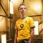 La camiseta amarilla de local del BVB de la temporada 26-27 para mujer, con cuello negro, el escudo del BVB y los logotipos de Vodafone y Polestar, lucida por una mujer vista de frente.