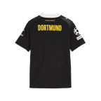 The BVB 26-27 away jersey for kids in black and yellow, back view featuring yellow “Dortmund” lettering and a Champions League badge on the sleeve.