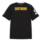 La camiseta de visitante del BVB para la temporada 2026/27, en negro y amarillo, vista desde atrás con la llamativa inscripción «DORTMUND» y el emblema de la Fundación UEFA en la manga.