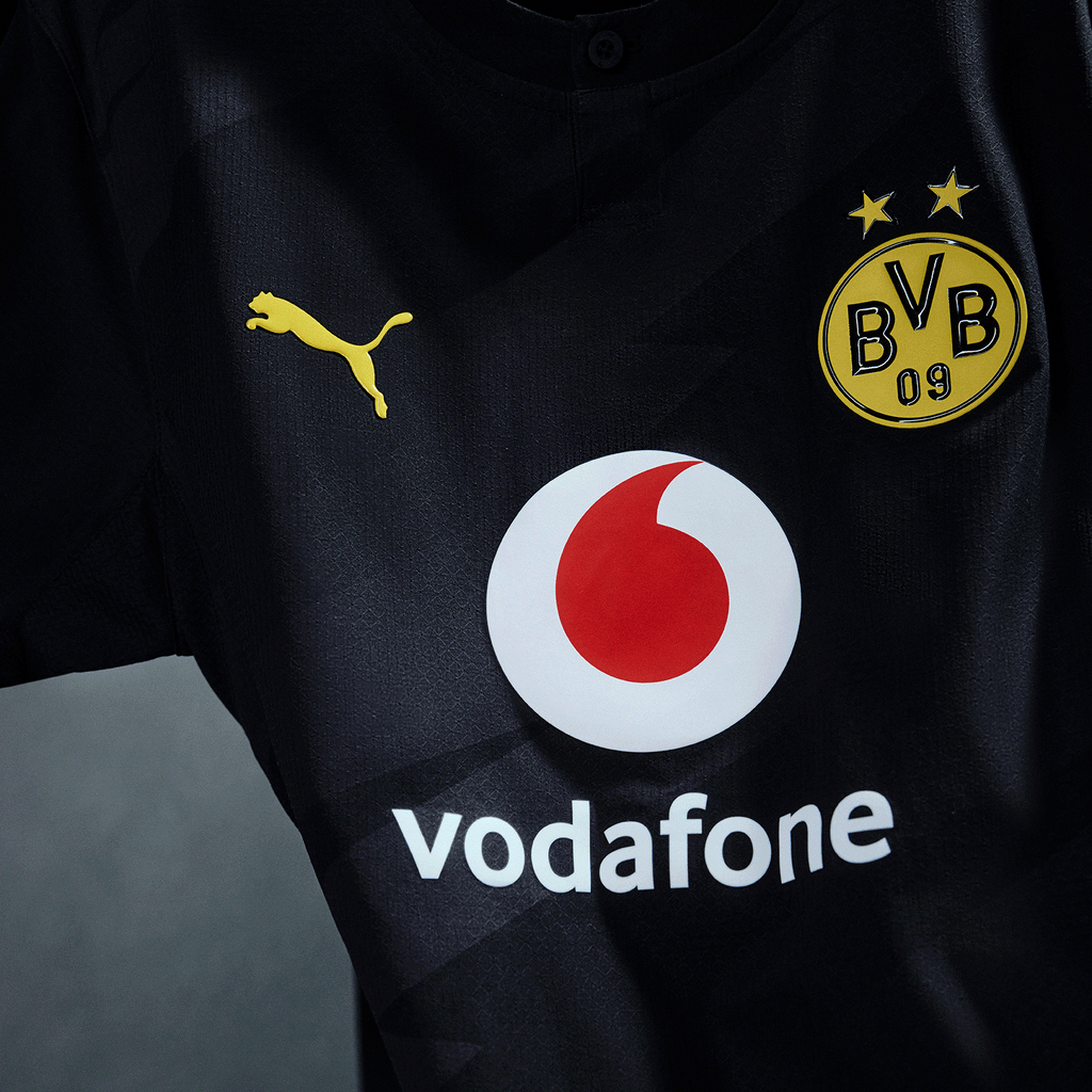 Detailaufnahme des schwarzgelben BVB Auswärtstrikots 26-27 mit PUMA-Logo, BVB-Emblem und Vodafone-Logo auf der Vorderseite.
