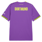 Vista trasera de la camiseta alternativa morada del BVB de la temporada 26-27, con la inscripción «Dortmund» en amarillo y rayas amarillas en las mangas.