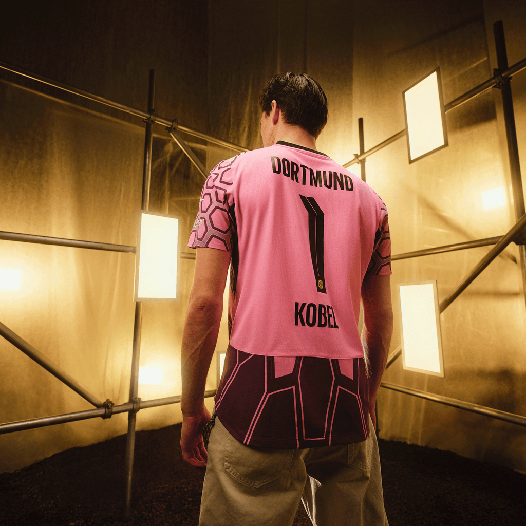Maglia da portiere del BVB viola della stagione 2026/2027 con la scritta nera "DORTMUND", il numero 1 e il nome "KOBEL" sul retro, presentata in un ambiente industriale.