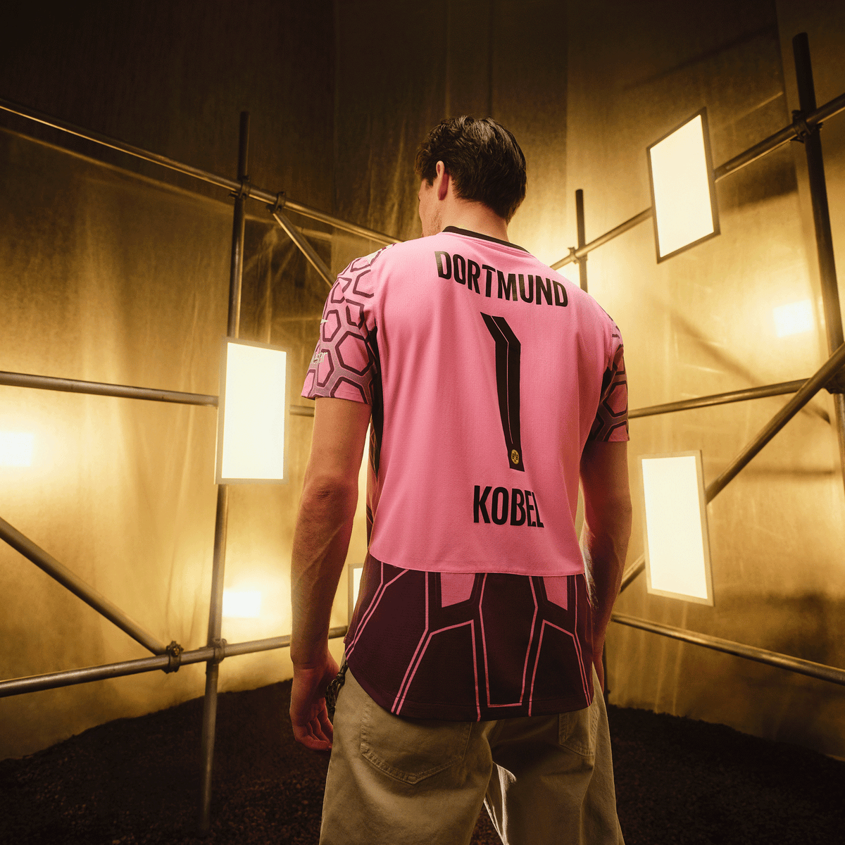 Maglia da portiere del BVB viola della stagione 2026/2027 con la scritta nera "DORTMUND", il numero 1 e il nome "KOBEL" sul retro, presentata in un ambiente industriale.